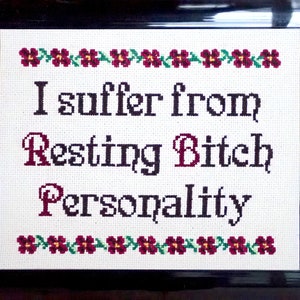 以下が含まれることがあります： 白い背景に赤い花が縁取られた額装されたクロスステッチ。テキストは「I suffer from Resting Bitch Personality」です。
