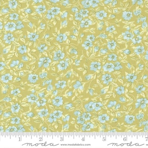 May include: A yellow fabric with a small blue floral pattern. The fabric is measured in inches with a ruler at the bottom of the image. The ruler has the word "moda" printed on it.