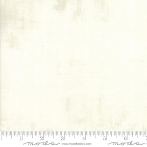 May include: Off-white fabric with subtle texture and a ruler along the bottom edge. The fabric has a slightly distressed appearance, with variations in tone across the surface. The fabric is suitable for quilting and other craft projects.