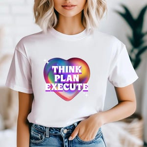 May include: White t-shirt with a colorful heart graphic that says "THINK PLAN EXECUTE" in purple text.