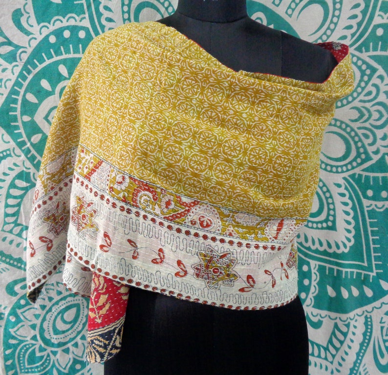 May include: A yellow and white kantha quilt scarf with a red and white floral border. The scarf is draped over a mannequin's shoulders.
