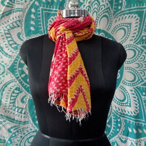 May include: A red and yellow kantha stitch scarf with a geometric pattern. The scarf is draped around a mannequin's neck.