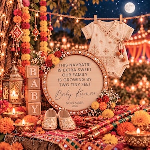 May include: A cream-coloured baby onesie with gold embroidery, a round wooden sign with the text 'THIS NAVRATRI IS EXTRA SWEET OUR FAMILY IS GROWING BY TWO TINY FEET Baby Kumar NOVEMBER 2026', wooden blocks spelling 'BABY', and small shoes.