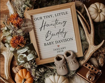 May include: A wooden framed sign with the text "OUR TINY, LITTLE Hunting Buddy BABY DAVISON JANUARY 2026" is surrounded by pumpkins, flowers, baby booties, and a sonogram. A vintage-style camera and deer antlers complete the rustic theme.