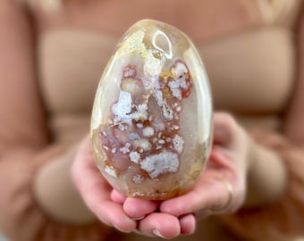 May include: A large, white agate geode with red and brown inclusions. The geode is smooth and polished, and it has a natural, organic shape.