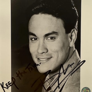 May include: Black and white photograph of a man smiling, with dark hair and a denim shirt. The image is signed with a black marker. Text includes "KEEP the Faith-" and "SHOWDOWN IN LITTLE TOKYO". Copyright information is at the bottom.