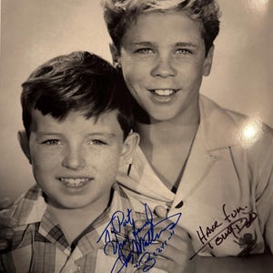 May include: Black and white photograph of two smiling young men. One has dark hair and a plaid shirt, the other has light hair and a button-down shirt. Both shirts are light-colored. The photo includes signatures in blue ink that read "Patty, Jerry Mathers, Beaver" and "Have fun. Tony Dow."
