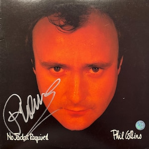 以下が含まれることがあります： 黒い背景に、オレンジ色の顔をしたフィル・コリンズのポートレートが特徴のアルバムカバー。「No Jacket Required」というアルバムタイトル、彼のサイン、アーティスト名が確認できます。