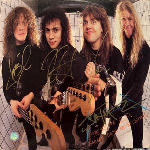 Op de afbeelding: Een foto van vier muzikanten met hun instrumenten. De afbeelding toont een basgitaar en elektrische gitaren. De bandleden dragen zwarte shirts en hebben lang haar. De albumhoes heeft handtekeningen en de tekst "Metallica" en "The $5.98 E.P. Garage Days Re-visited."