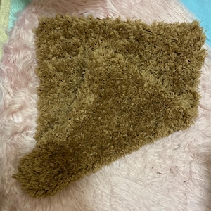 May include: A brown, shaggy rug with a rectangular shape and a smaller, attached rectangular extension. The rug has a thick, textured pile and is set against a pink, fluffy background. The rug's color is a warm, earthy tone.