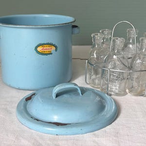 May include: A light blue enamel pot with a matching lid and a set of small glass bottles in a metal carrier. The pot has two handles and a label that reads "Doll E Toys Amsco". The lid has a handle and some rust.