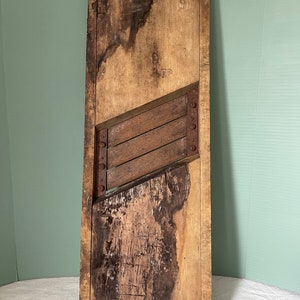 May include: A vintage wooden food slicer with a rusted metal blade. The wood is weathered and has a dark brown patina. The slicer is approximately 18 inches tall.