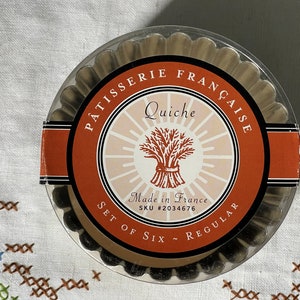 May include: A set of six silver-colored, regular-sized, metal quiche pans with a red, black, and white label that reads "Patisserie Française Quiche Made in France SKU #2034676 Set of Six - Regular".