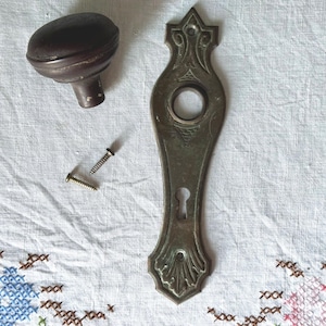 May include: Antique brass door hardware set with a decorative backplate and a round knob. The backplate has a keyhole and intricate details. The knob is brown and has a smooth surface.