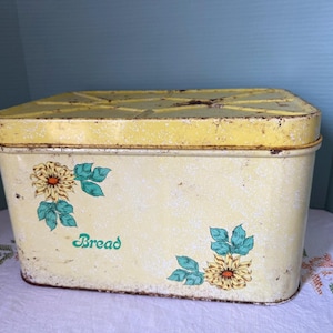 May include: Vintage yellow bread box with a matching lid. The box features floral decals with yellow and orange flowers and teal leaves. The word "Bread" is written in green script on the front.