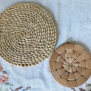 May include: Two round woven placemats, one made of natural straw and the other made of light brown wood.