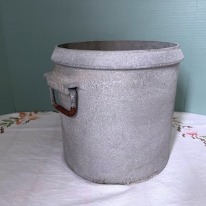 May include: A gray metal pot with a single handle. The handle is made of metal and has a rusty brown color.