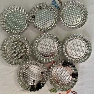 May include: Eight silver-colored metal tart pans with fluted edges and a dimpled bottom. The pans are arranged in a circle on a white surface.