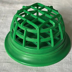 May include: Green plastic floral frog with a dome-shaped grid for holding flowers.