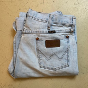May include: A pair of light blue denim jeans with a brown leather Wrangler patch on the back pocket.