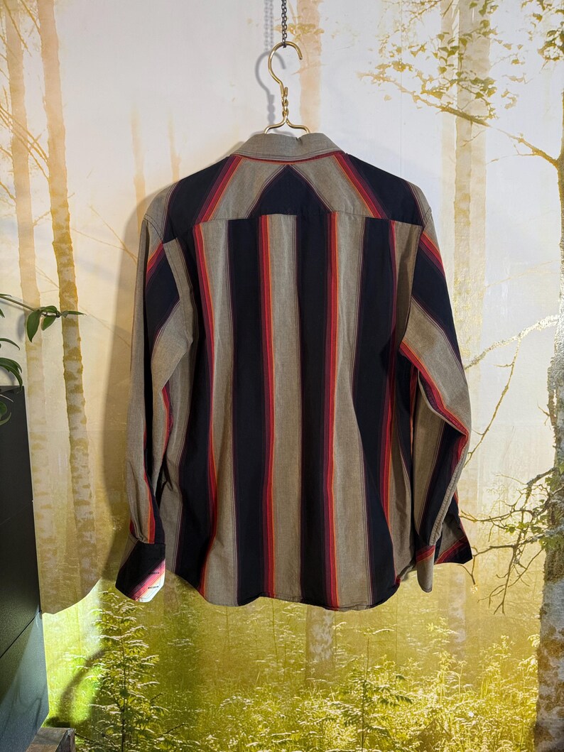 May include: A long-sleeved button-down shirt with vertical stripes in shades of red, black, and brown on a beige background.