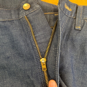 May include: Close-up of a blue denim zipper fly with a gold zipper and a "Wrangler" button. The zipper has a "TALON" label.