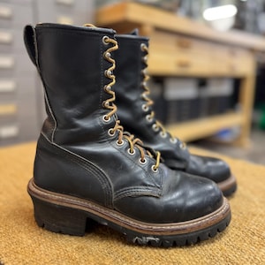 May include: A pair of black leather lace-up boots featuring a high-top design, silver-toned metal eyelets, and tan laces. The boots have a thick, dark brown stacked heel and a rugged black rubber lug sole with visible stitching along the welt.