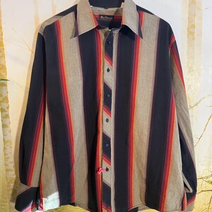 May include: A long-sleeved button-down shirt with vertical stripes in shades of black, red, orange, and gray. The shirt has a pointed collar and a button-up front.