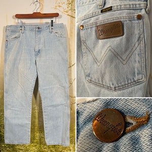 Puede incluir: Vaqueros de mezclilla azul claro con un parche de cuero marr&oacute;n Wrangler en el bolsillo trasero. Los vaqueros tienen una pierna recta y un ajuste holgado.