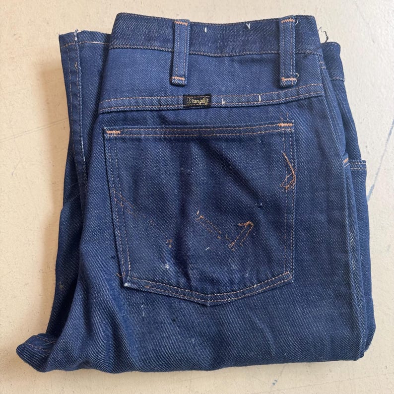 May include: A pair of dark blue denim jeans with a back pocket and a Wrangler label.