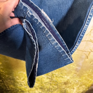 Pu&ograve; includere: Primo piano dell'interno di un paio di jeans in denim blu. I jeans hanno una cucitura blu scuro lungo l'interno della gamba.