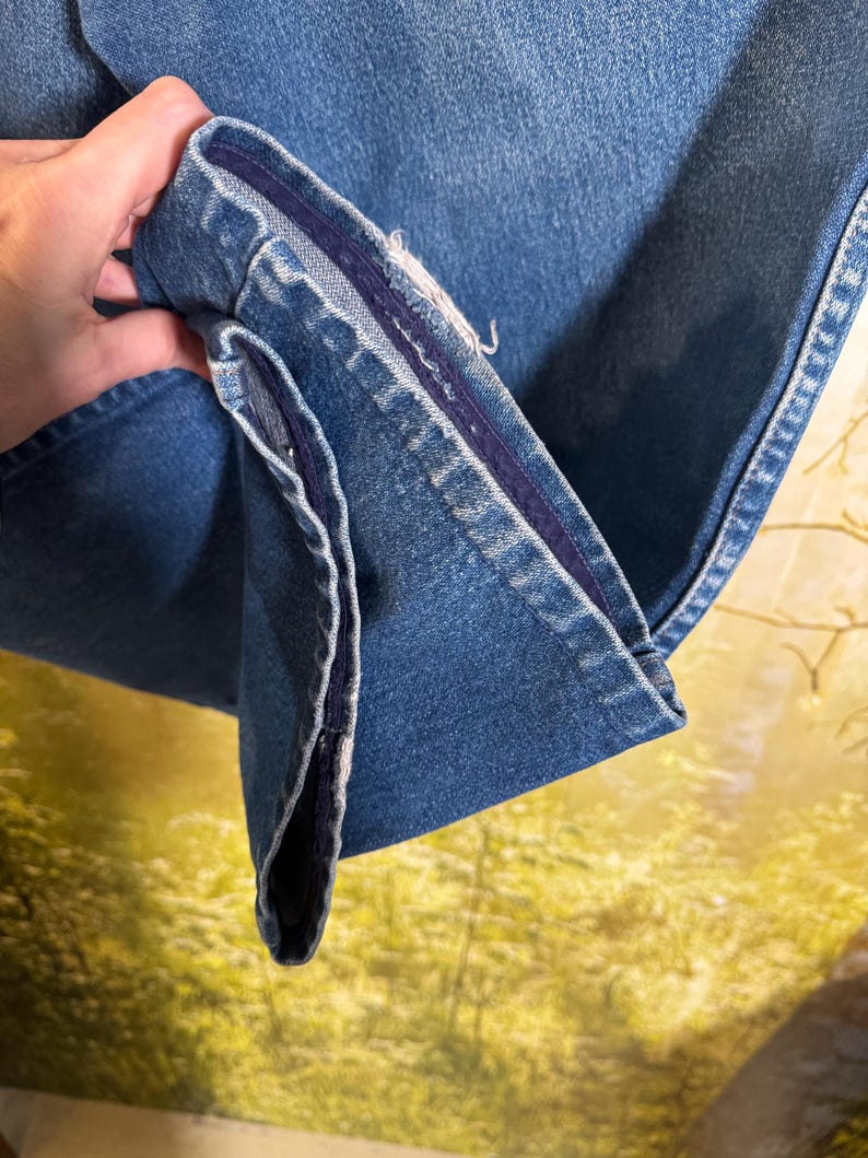Pu&ograve; includere: Primo piano dell'interno di un paio di jeans in denim blu. I jeans hanno una cucitura blu scuro lungo l'interno della gamba.