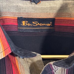 May include: A black and brown striped button-down shirt with a black collar and a label that reads "Ben Sherman".