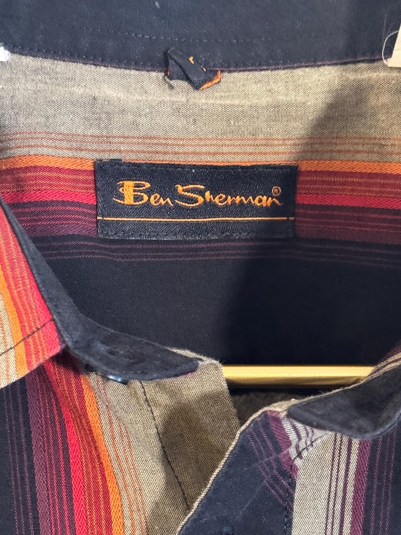 May include: A black and brown striped button-down shirt with a black collar and a label that reads "Ben Sherman".