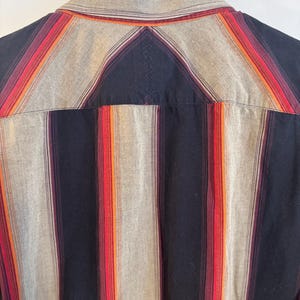 May include: A striped button-down shirt with a black, gray, orange, and red color scheme. The shirt has a classic collar and long sleeves.