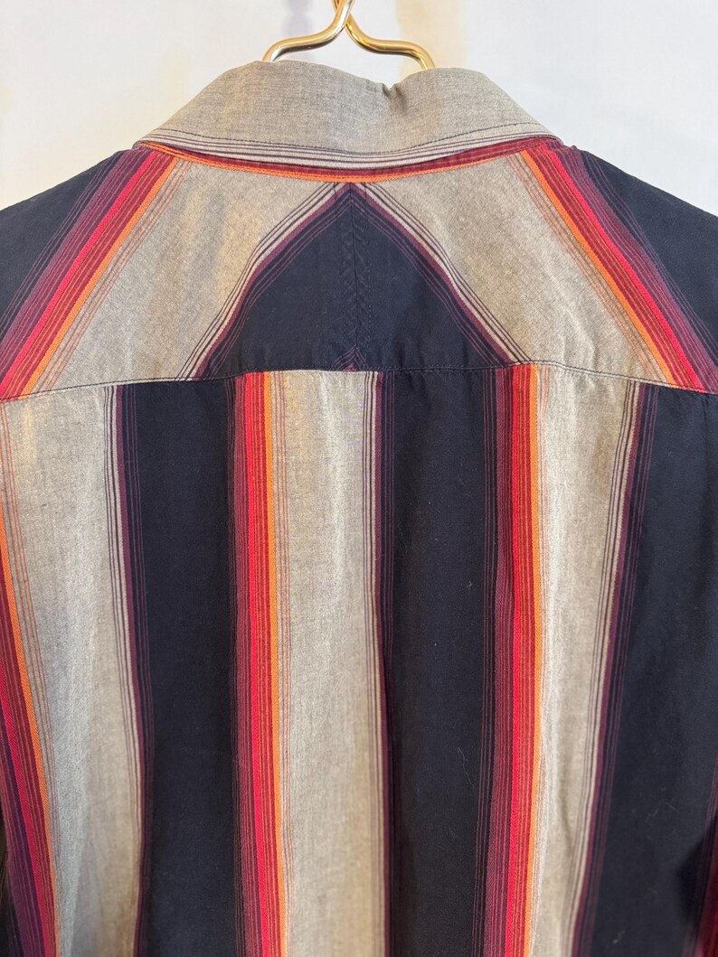 May include: A striped button-down shirt with a black, gray, orange, and red color scheme. The shirt has a classic collar and long sleeves.