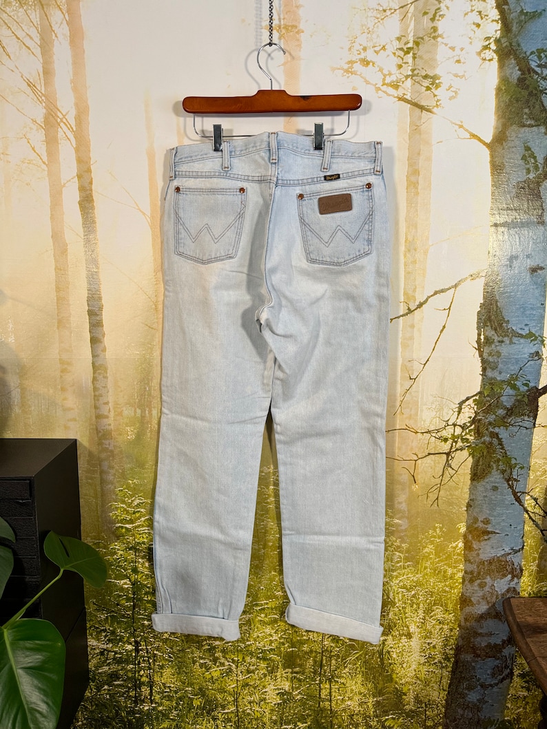 May include: Light blue denim jeans with a cuffed hem. The jeans have a brown leather patch with the Wrangler logo on the back.