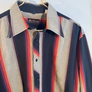May include: A long-sleeved button-down shirt with a striped pattern in shades of black, red, orange, and gray. The shirt has a collar and a label that reads "Ben Sherman".