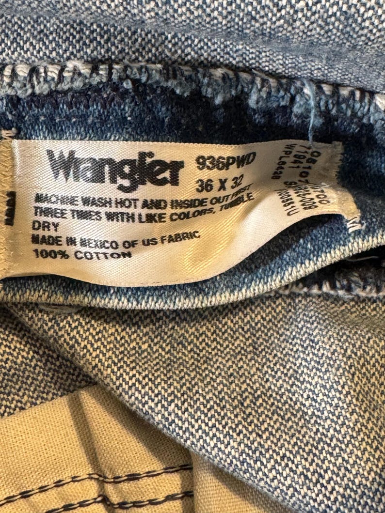 Pu&ograve; includere: Un'etichetta bianca con testo nero che recita "Wrangler 936PVD 36 x 32" e "MACHINE WASH HOT AND INSIDE OUT FIRST THREE TIMES WITH LIKE COLORS, TUMBLE DRY MADE IN MEXICO OF US FABRIC 100% COTTON".