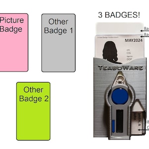 May include: Three badges, one with a picture, one with the text "MAY2024", and one with the text "John Smith, A". The badges are in a gray plastic badge holder with a blue button and a silver key ring.