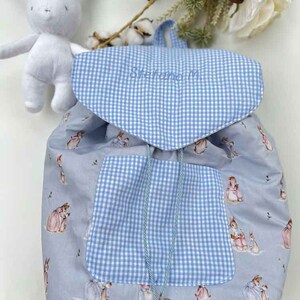 Può includere: Uno zaino in tessuto gingham blu e bianco con stampa Peter Rabbit. Lo zaino ha una grande tasca sul davanti e una chiusura con coulisse.