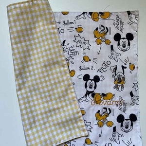 Può includere: Tessuto reversibile con un motivo a quadri giallo e bianco da un lato e una stampa di cartoni animati dall'altro. Il lato del cartone animato presenta illustrazioni di Topolino e Pluto con fumetti e testo.