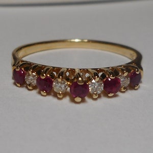 May include: A gold band ring with a row of red rubies and diamonds.