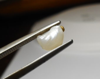 May include: A white pearl with a gold bead at the top, held by tweezers.