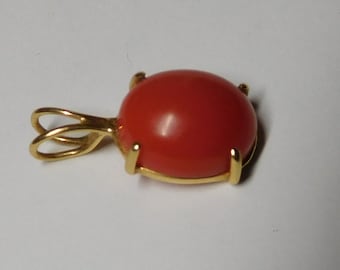 Può includere: Un pendente in oro con una vivace gemma rossa di forma ovale. La gemma è tenuta in posizione da quattro griffe d'oro, con un anello d'oro per una catena. Il pendente è posto su uno sfondo bianco.