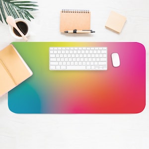 May include: A colourful gradient desk mat with a white keyboard and mouse on top. The mat is a vibrant mix of blue, green, yellow, orange, and pink.