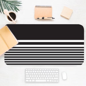 May include: Black and white striped desk mat with a black top section. The mat is on a white surface with a keyboard, mouse, and other office supplies.