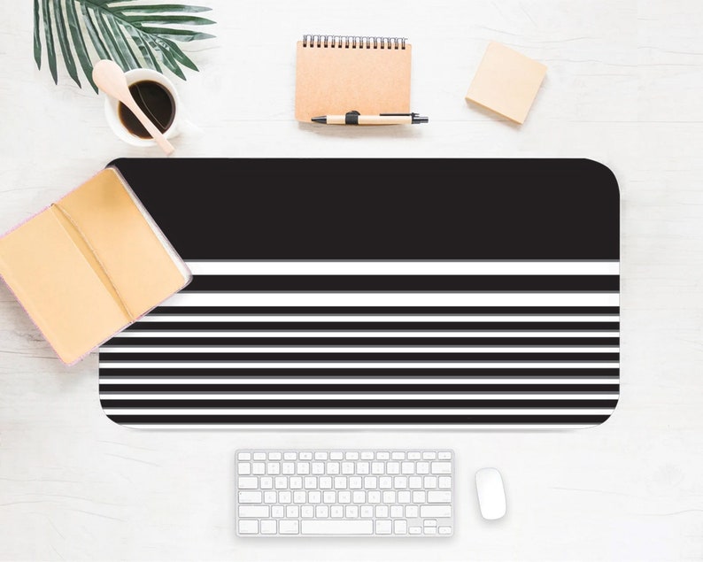 May include: Black and white striped desk mat with a black top section. The mat is on a white surface with a keyboard, mouse, and other office supplies.