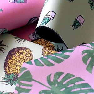 May include: Close-up of three different fabric swatches with tropical patterns. The first swatch is pink with a green cactus and a pineapple design. The second swatch is green with a white potted cactus design. The third swatch is pink with a green monstera leaf design.