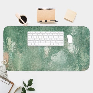 May include: A green and white abstract desk mat with a white keyboard and mouse on top. The desk mat is made of a textured material and has a faded, vintage look.